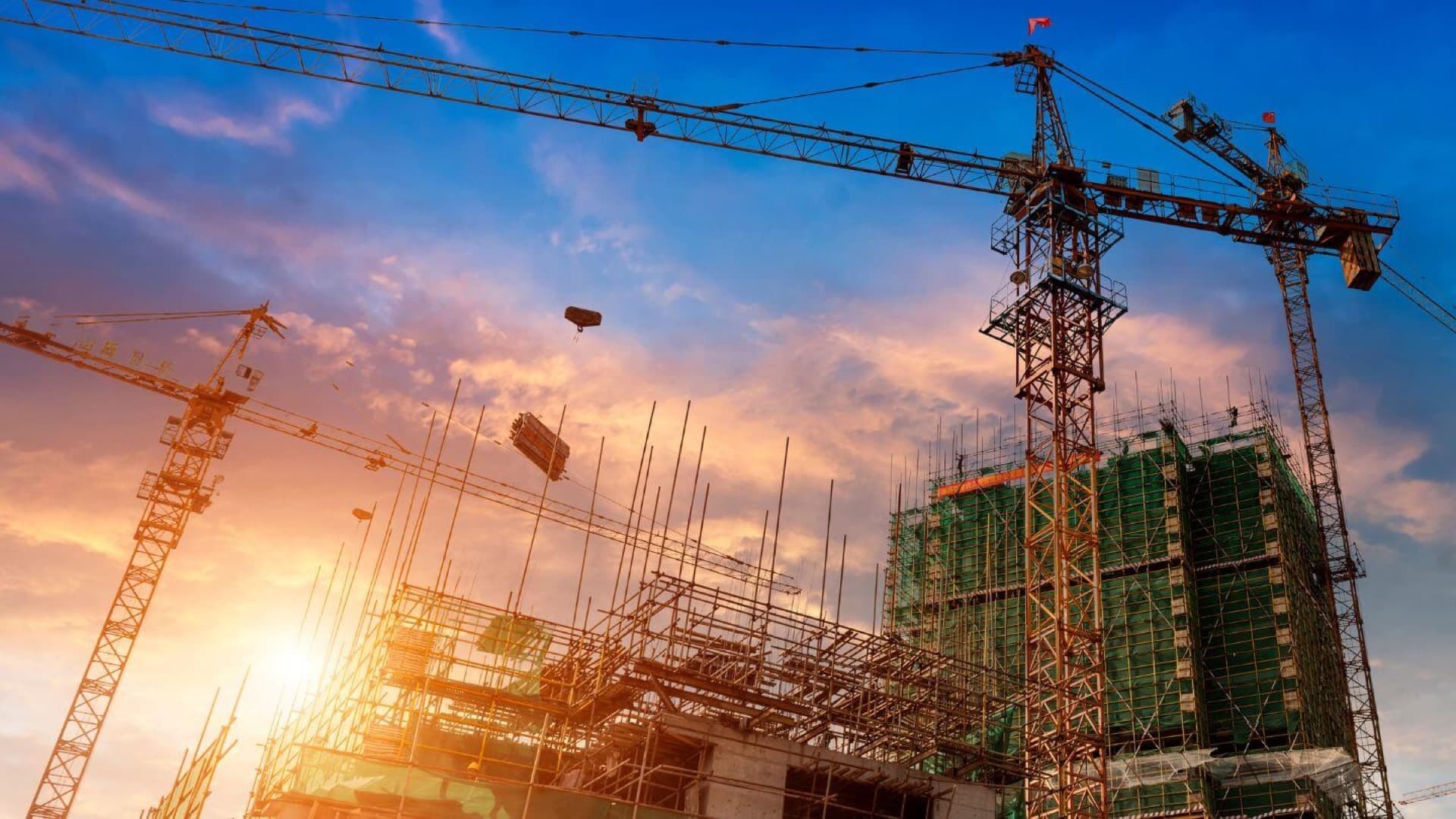 Tower cranes over a building under construction at sunset